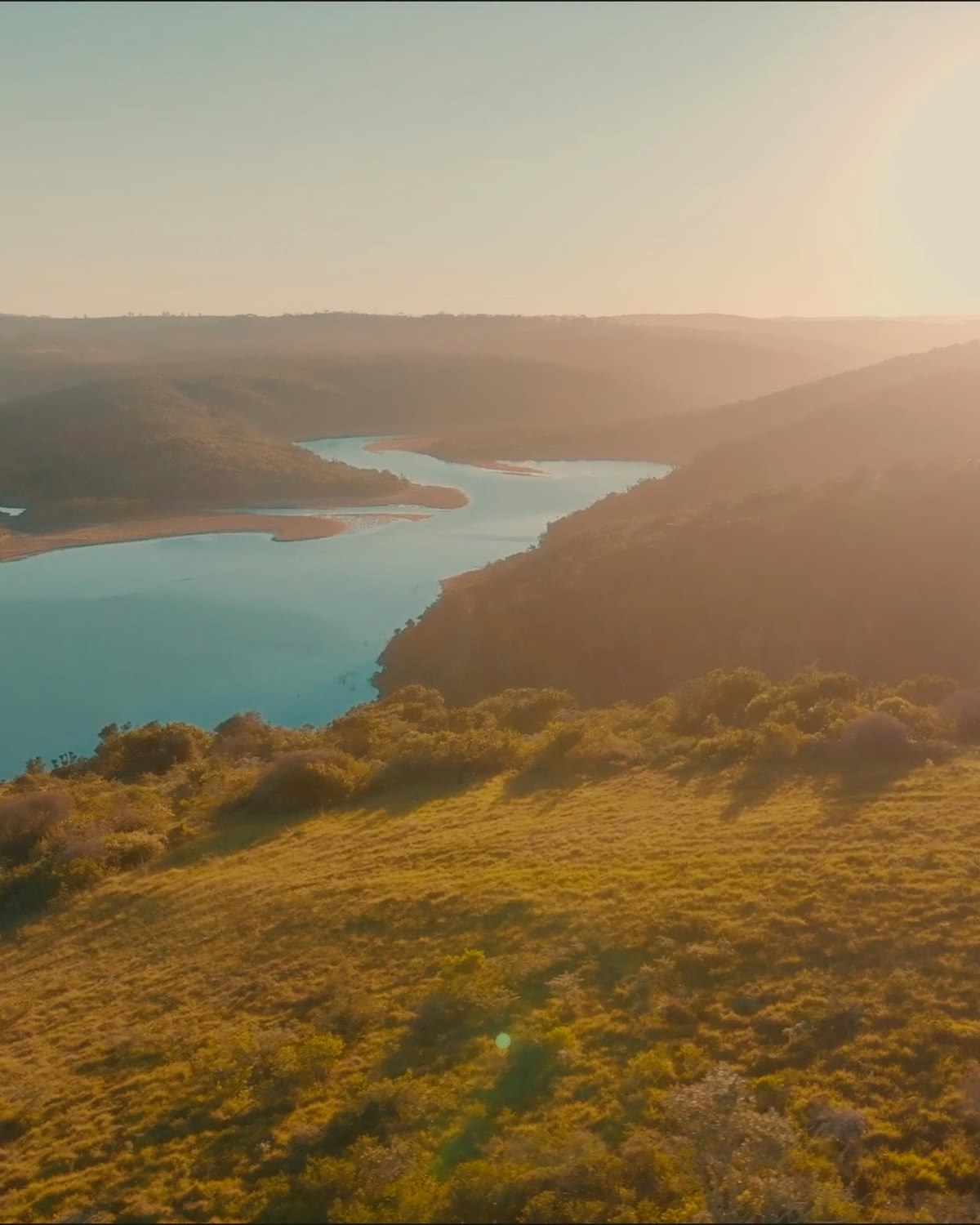 A game-drive vehicle resting on a grassy ridge above the river valley at sunrise, the sun low over the reserve hills